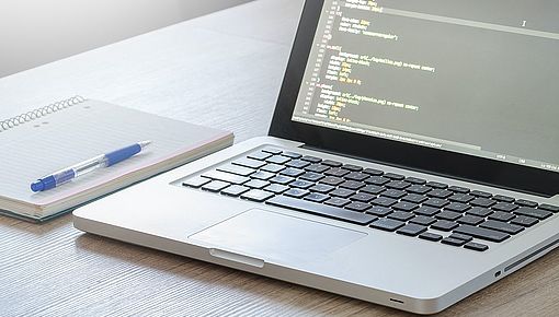 Laptop mit Programmiersprache auf dem Bildschirm, Notizheft und Stift