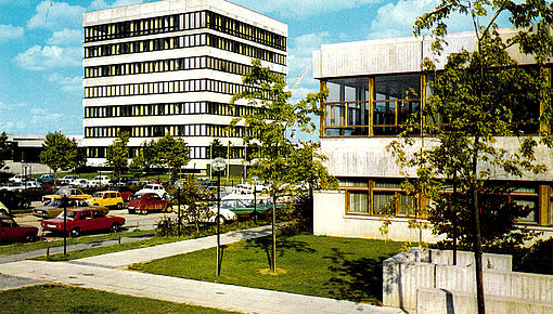 Farbfoto mehrerer Universitätsgebäude und eines Parkplatzes