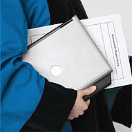 Eine Person trägt einen Talar in der Farbe der Fakultät für Chemie und Pharmazie, in der Hand hält sie einen Laptop um eine Umlaufmappe der Universität Regensburg