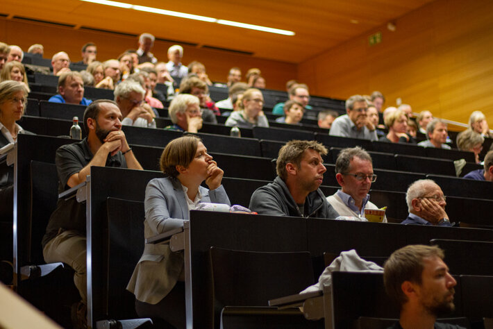 In einem Hörsaal mit ansteigenden Stuhlreihen sitzen viele Personen. (öffnet Vergrößerung des Bildes)