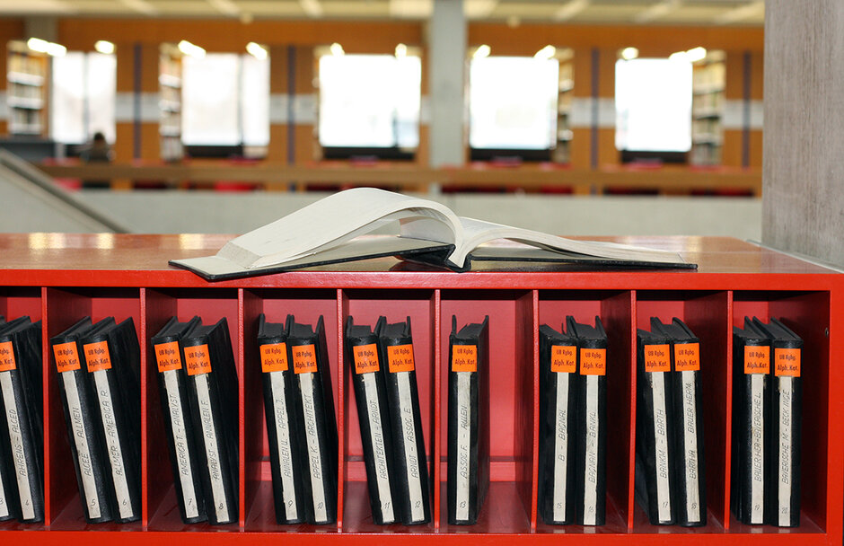 Schwarz gebundene Bände im Regal, im Hintergrund helle Buchregale