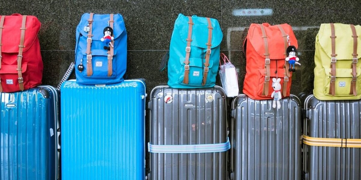 Man sieht fünf Koffer in blau und schwarz nebeneinander aufgereiht. Auf den Koffern liegen Rücksäcke in verschiedenen Farben. 