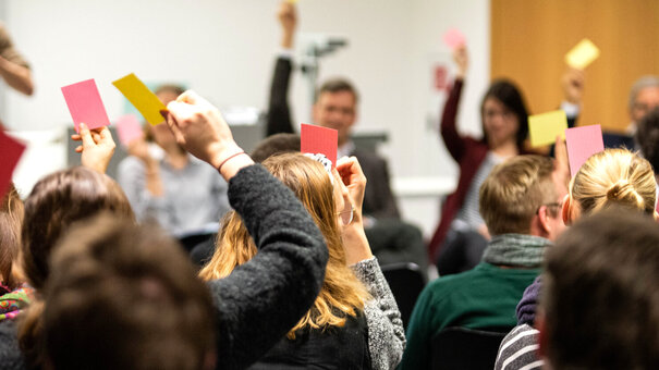 In einem Seminarraum halten Menschen farbige Karten in gelb oder rot zur Abstimmung in die Höhe. 