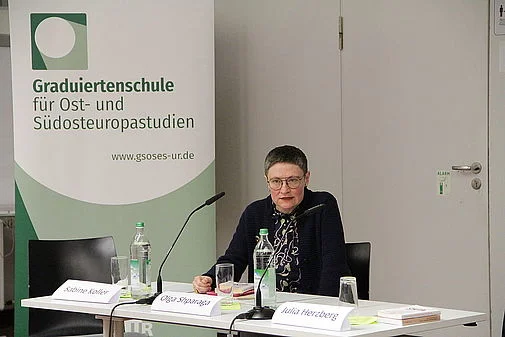 Frau Dr. Olga Shparaga sitzt hinter einem Rednerpult mit Mikrofon.