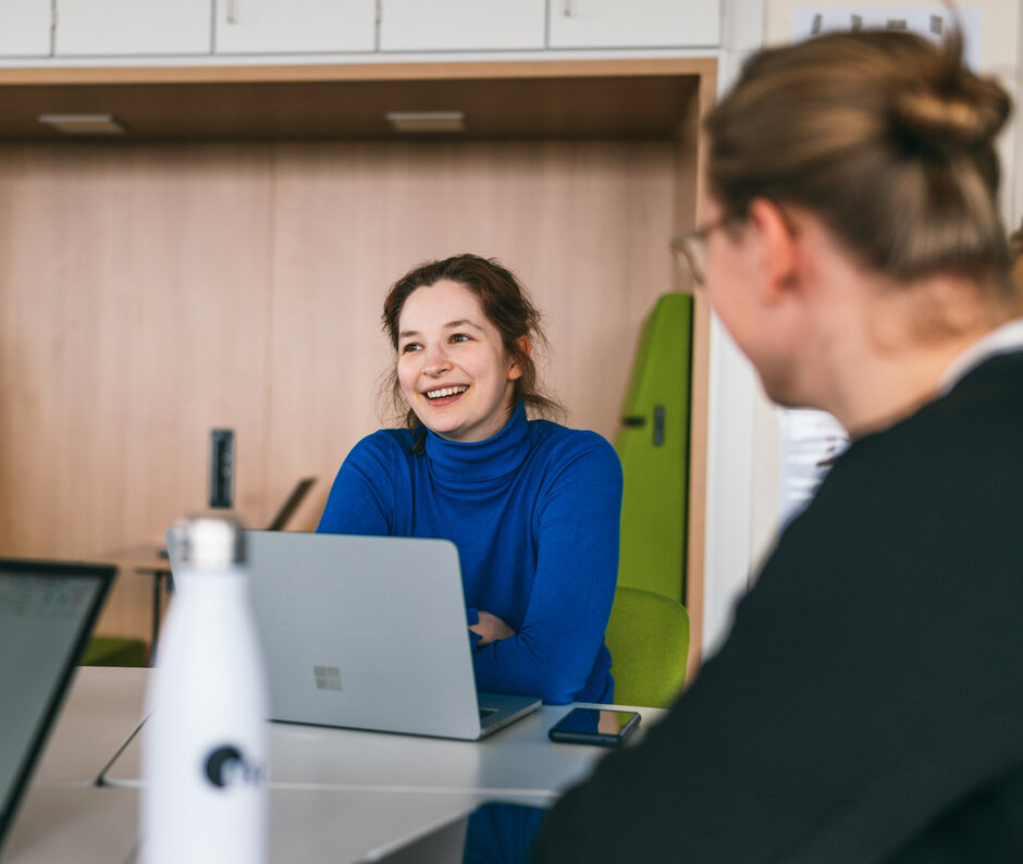 Eine Studentin sitzt lächelnd und konentriert zusammen mit anderen Studierenden an einem Seminartisch
