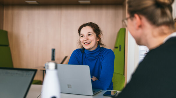 Eine Studentin sitzt lächelnd und konentriert zusammen mit anderen Studierenden an einem Seminartisch