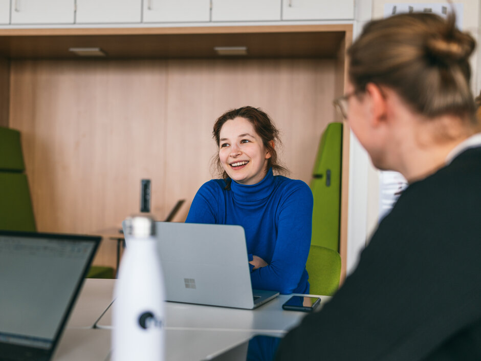 Eine Studentin sitzt lächelnd und konentriert zusammen mit anderen Studierenden an einem Seminartisch