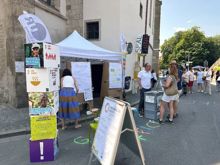 Ein Informationsstand mit Plakataufstellern, einem Pavillion und Beachflags auf einer Straße vor einem historischen Gebäude. (öffnet Vergrößerung des Bildes)