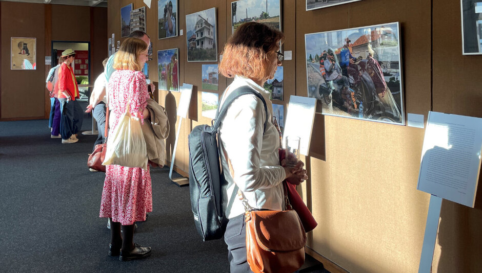 Mehrere Personen stehen in einem hellen Raum und betrachten Fotografien, die an der Wand befestigt sind. (opens enlarged image)