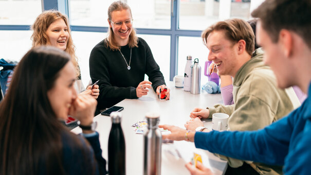 Eine Gruppe Studierender spielt Karten an einem Tisch in einer Cafeteria.