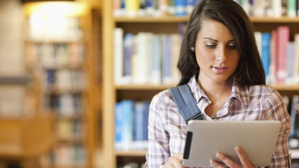 Frau mit Tablet vor Bücherregal.