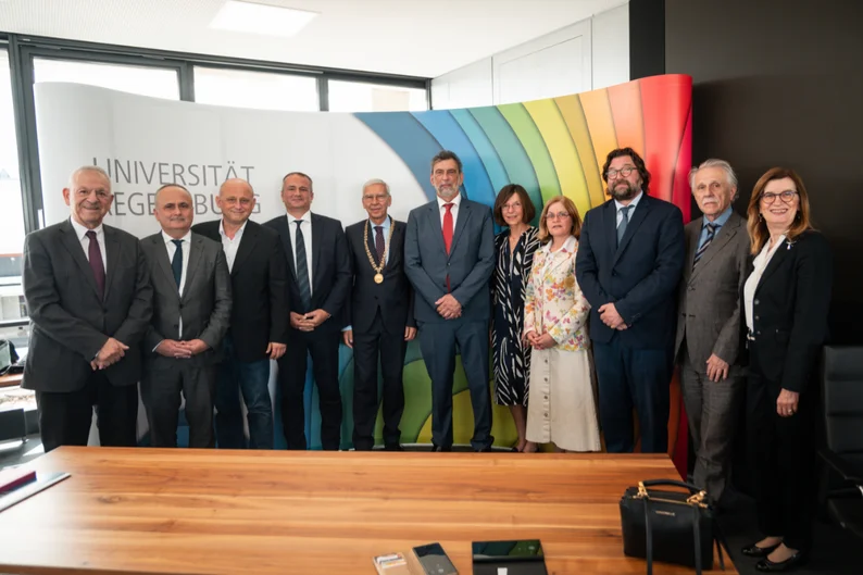 11 Personen haben sich in einem Konferenzsaal für ein Gruppenfoto in einer lockeren Reihe aufgestellt.  (öffnet Vergrößerung des Bildes)