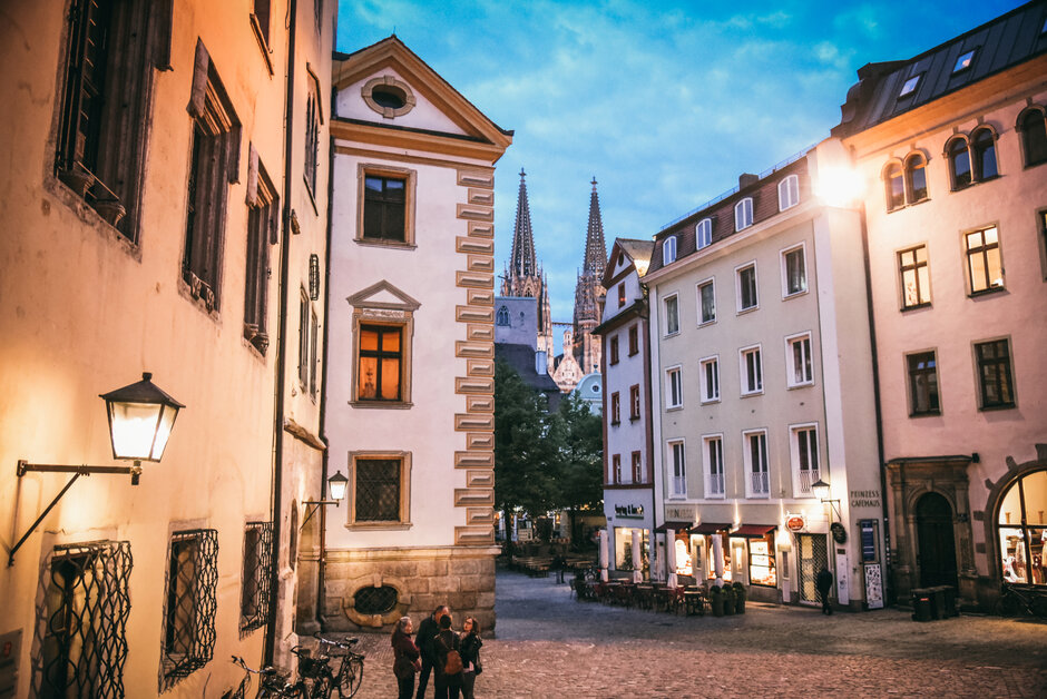 Abenstimmung in einer Altstadtgasse mit historischen Häusern. In der Ferne erkennt man die Spitzen eines gotischen Kirchturms.
