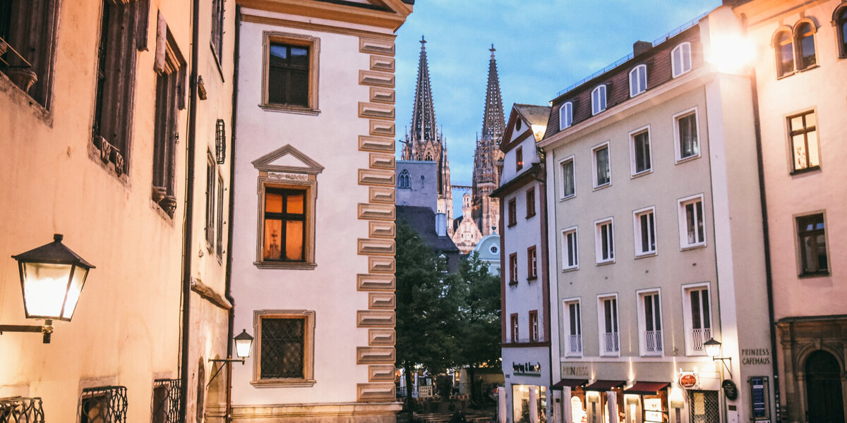 Abenstimmung in einer Altstadtgasse mit historischen Häusern. In der Ferne erkennt man die Spitzen eines gotischen Kirchturms.