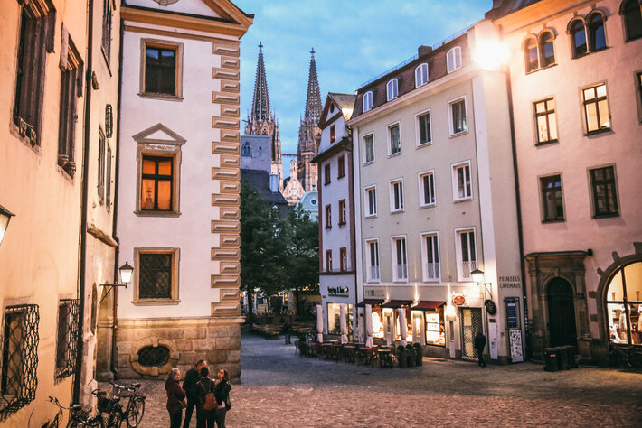 Abenstimmung in einer Altstadtgasse mit historischen Häusern. In der Ferne erkennt man die Spitzen eines gotischen Kirchturms. (öffnet Vergrößerung des Bildes)