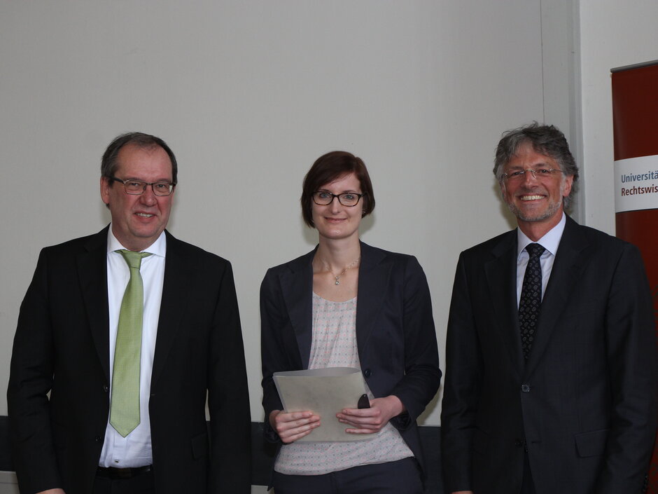Das Bild zeigt Dr. Anna Käsbauer, eine Urkunde haltend, bei der Preisverleihung mit den Professoren Preis (Köln) und Waltermann (Bonn). Rechts steht ein Aufsteller mit dem Logo der Juristischen Fakultät der Universität Köln. (öffnet Vergrößerung des Bildes)