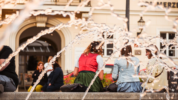 Junge Menschen sitzen in ein Gespräch vertieft am Rand eines Springbrunnens