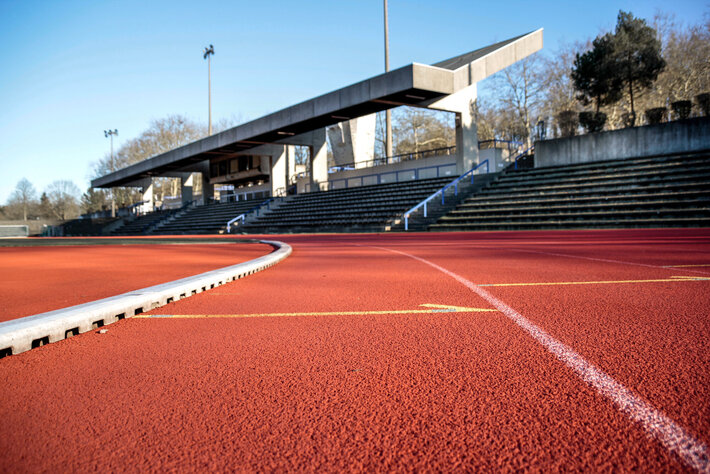 Nahaufnahme der Tartanbahn im Sportzentrum der Universität Regensburg, im Hintergrund die Zuschauertribüne (öffnet Vergrößerung des Bildes)