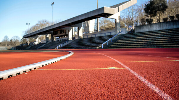 Nahaufnahme der Tartanbahn im Sportzentrum der Universität Regensburg, im Hintergrund die Zuschauertribüne