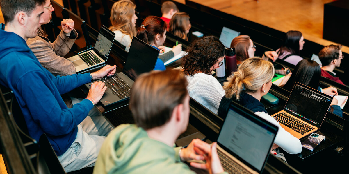 Man sieht einen Vorlesungssaal, in dem Studierende sitzen. 