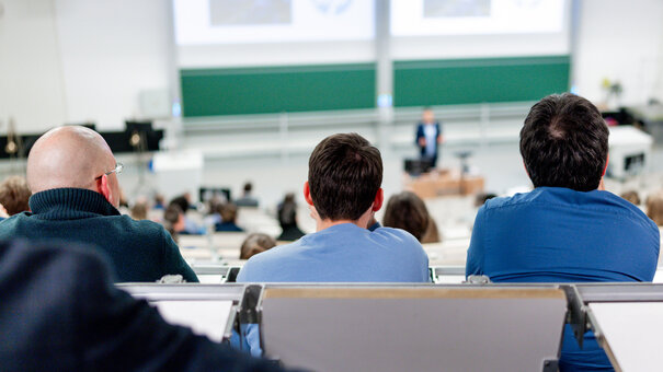 Blick auf drei Hinterköpfe in einem gut besuchten Hörsaal