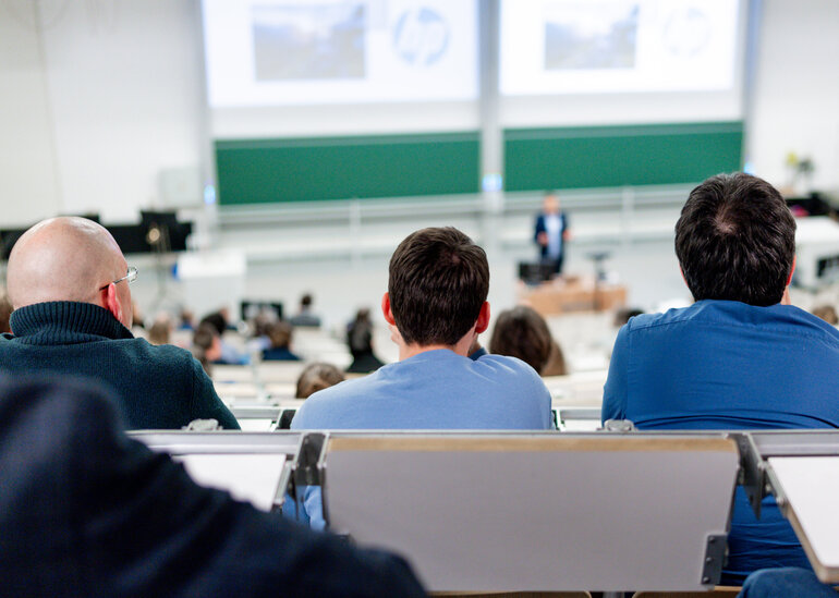 Blick auf drei Hinterköpfe in einem gut besuchten Hörsaal