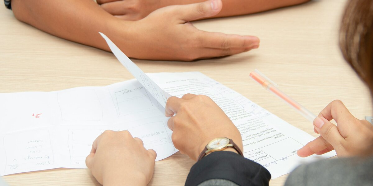 Man sieht mehrere Personen an einem Tisch, die Papiere in der Hand haben.