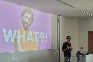 Ein Mann mittleren Alters steht vor einer Power-Point-Folie und hält einen Vortrag. 