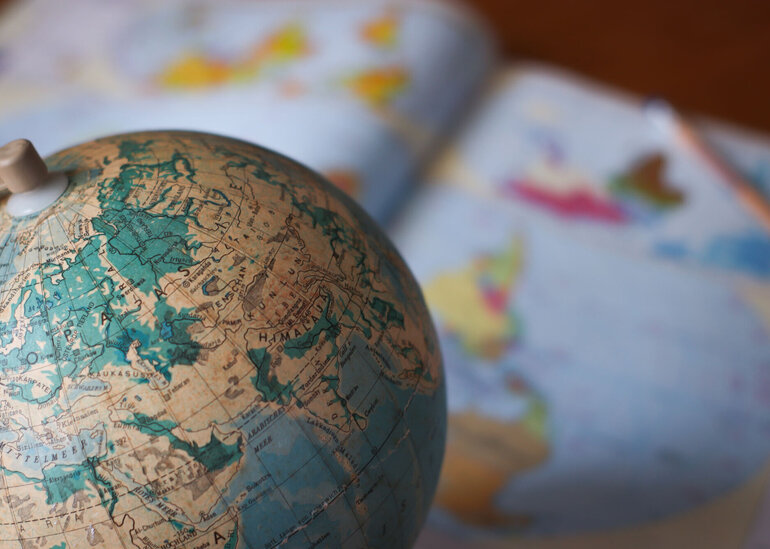 Nahaufnahme eines Globus, darunter verschwommen ein aufgeschlagener Atlas.