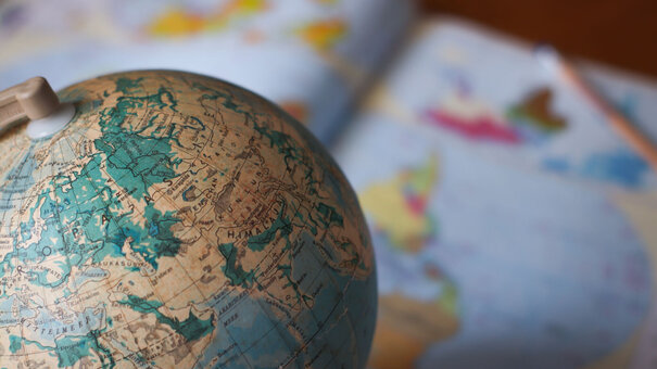 Nahaufnahme eines Globus, darunter verschwommen ein aufgeschlagener Atlas.