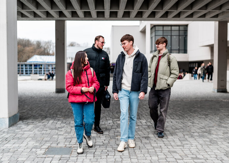 Vier Studierende gehen über den Campus der Universität Regensburg.