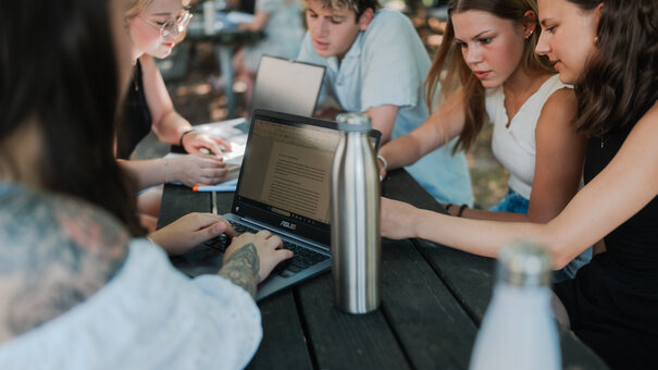 Studierende lernen und arbeiten gemeinsam an einem Tisch unter freiem Himmel