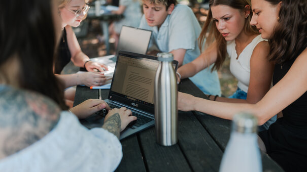 Studierende lernen und arbeiten gemeinsam an einem Tisch unter freiem Himmel