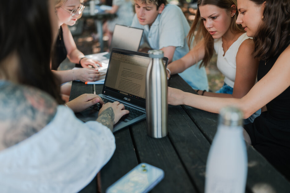 Studierende lernen und arbeiten gemeinsam an einem Tisch unter freiem Himmel