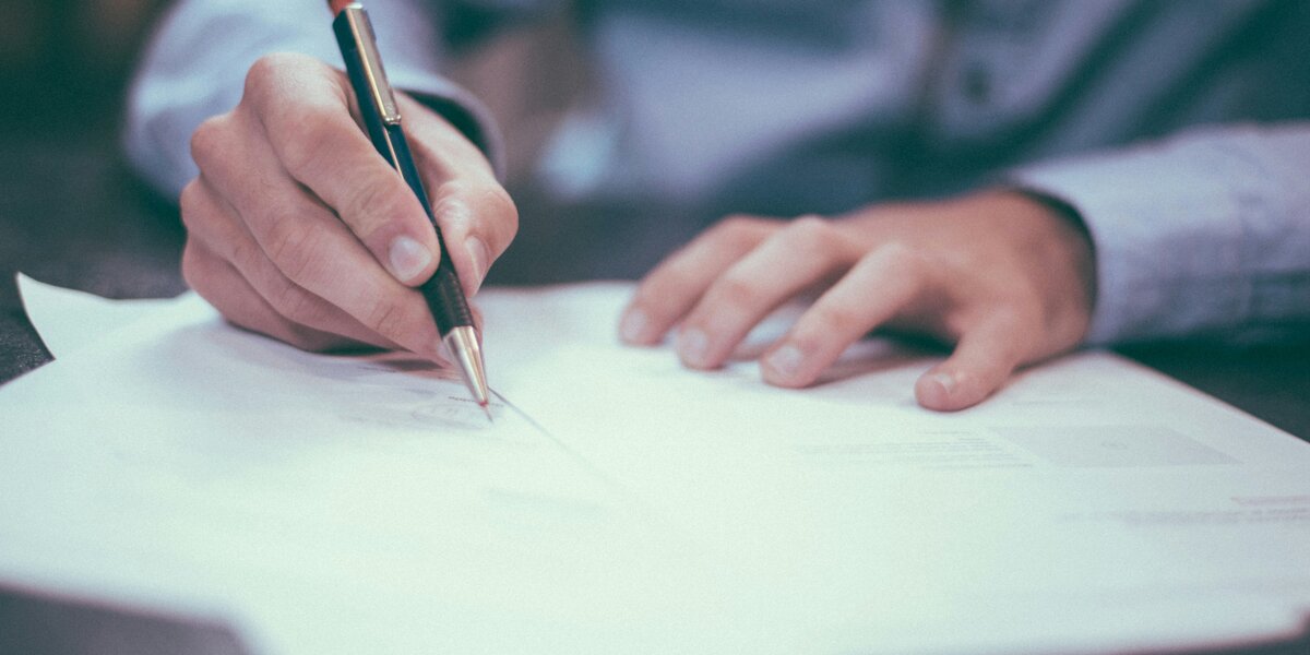 Ein Mann sitzt an einem Tisch und schreibt mit einem Kugelschreiber auf verschiedene Dokumente.