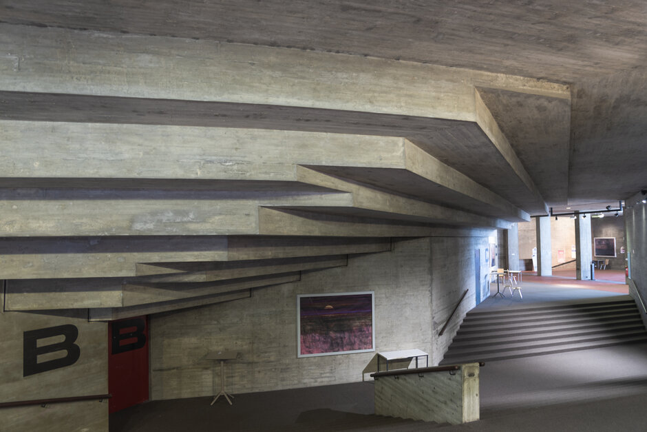 Ein Innenraum eines brutalistischten Hochschulgebäudes in Sichtbetonbauweise mit einer kühnen, verschachtelten Deckenkonstruktion (öffnet Vergrößerung des Bildes)