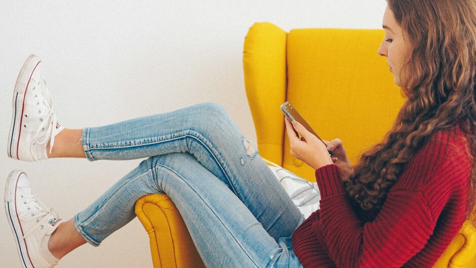 Young woman in a comfortable armchair, reading on her mobile phone