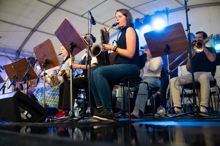 Das Uni-Jazzorchester Regensburg bei seinem Auftritt: Junge Menschen sitzen auf der Bühne und spielen Blasinstrumente (Saxophon und Posaune). (öffnet Vergrößerung des Bildes)