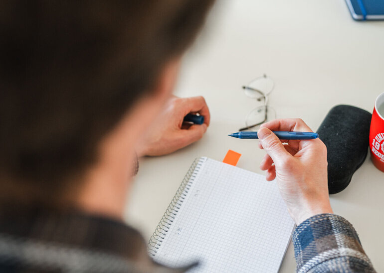 Person schreibt etwas in einen Notizblock