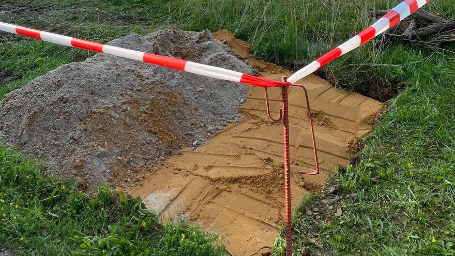 Square excavated section in the meadow, cordoned off by a barrier tape