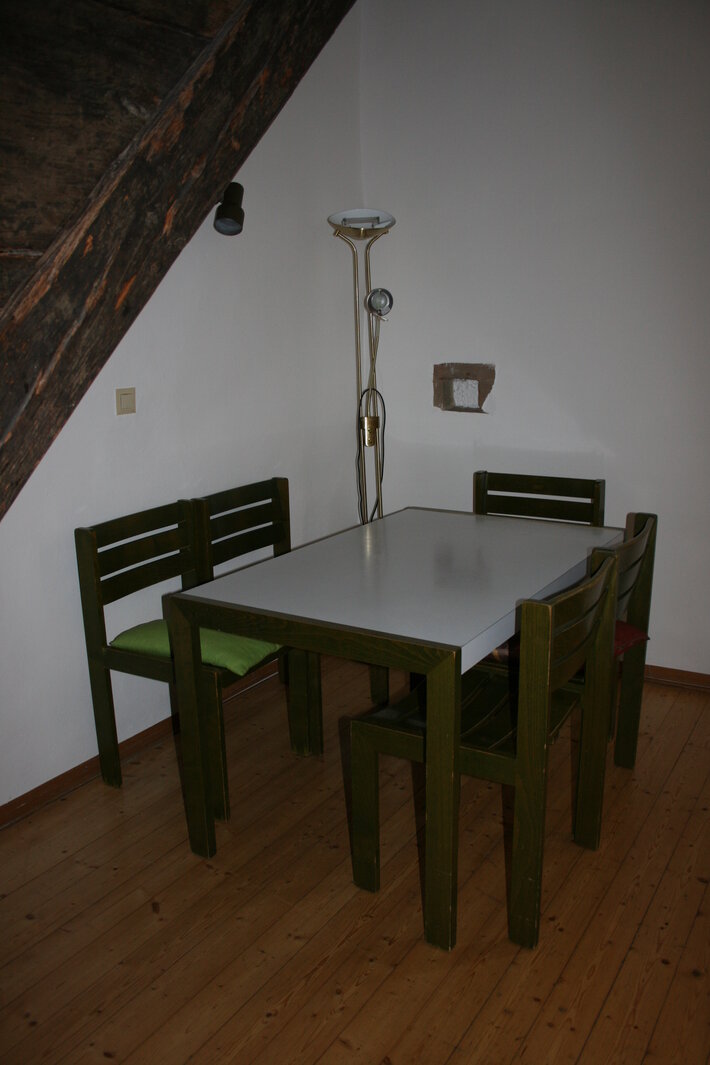 Inneneinrichtung der Wohnung mit einem Tisch und vier Stühlen unter einem Treppenaufgang (öffnet Vergrößerung des Bildes)