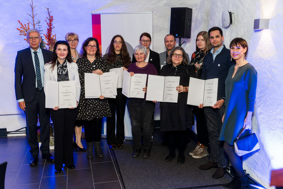 Eine Personengruppe steht in zwei Reihen, die Frauen in der vorderen Reihe halten Urkunden ins Bild.