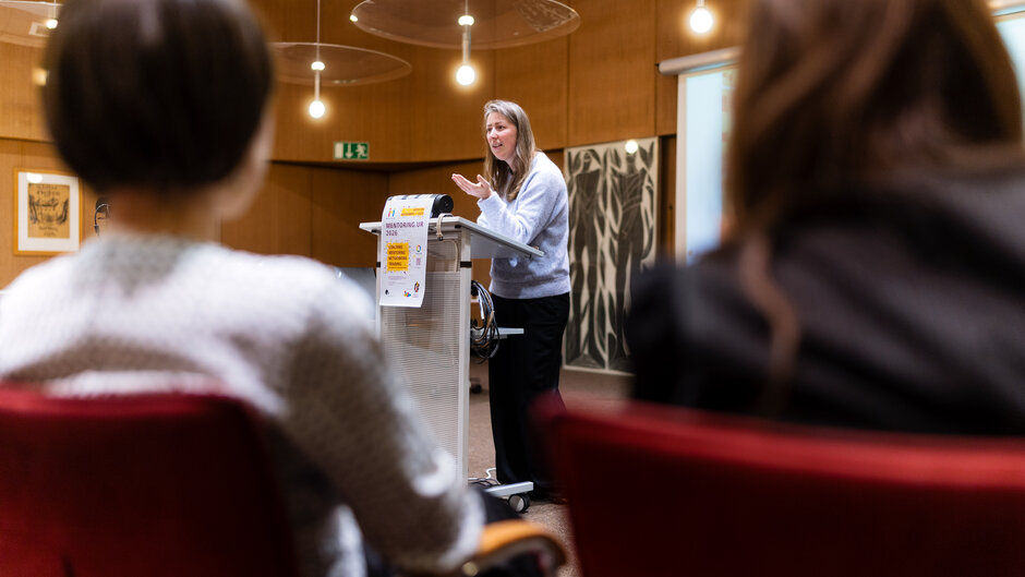 Frau mit langen Haaren, steht an Rednerpult, im Vordergrund Zuhörerinnen. (öffnet Vergrößerung des Bildes)