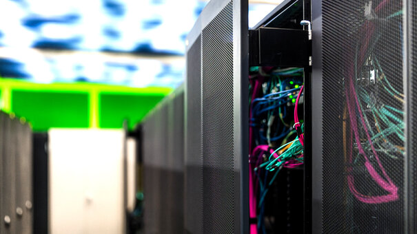 Eine Reihe von Schränken in einem Serverraum; einer davon ist halb geöffnet und gibt den Blick auf bunte Kabel frei.