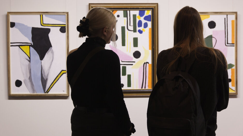 Zwei Frauen betrachten abstrakte Kunstwerke.