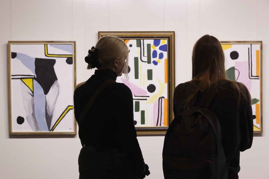 Zwei Frauen betrachten abstrakte Kunstwerke.