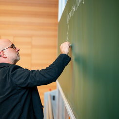 Ein Mann schreibt mit Kreide an eine Tafel in einem Hörsaal