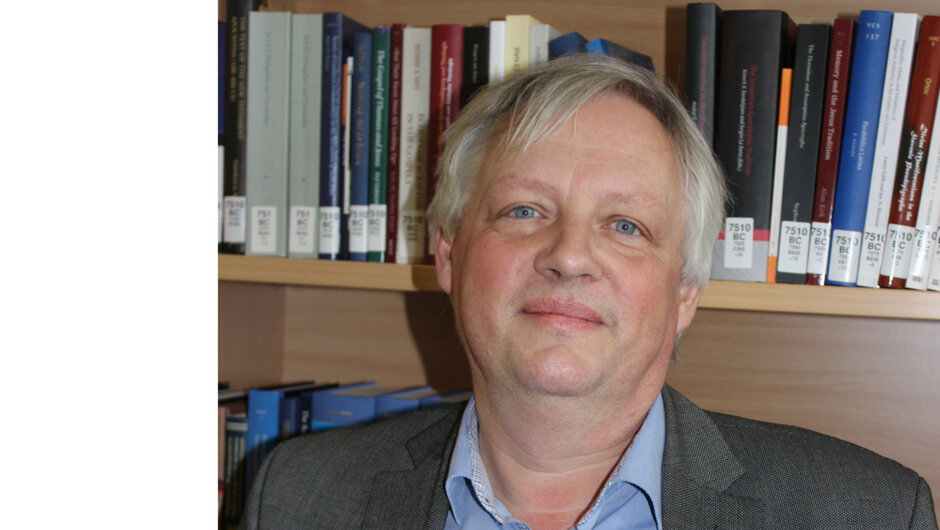 Porträtfoto eines Mannes, der vor einem Bücherregal steht.