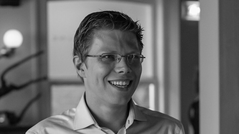 Schwarz-weiß-Porträt eines lächelnden Mannes mit kurzem Haar und Brille.