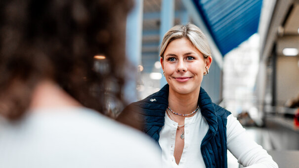 Zwei Studentinnen sitzen einander zugewandt an einem langen, thekenartigen Tisch. Neben ihnen stehen zwei Trinkflaschen.
